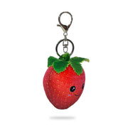 Angle view of a plush strawberry keychain with red fabric, yellow seed details, green felt leaves on top, and a silver key ring clip, on a white background.
