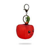 Angled side view of a red plush apple-shaped keychain with stitched smiling face, green leaf and brown stem on top, and a silver key ring clip, on a white background.