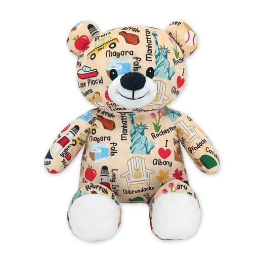 Front view of a tan plush teddy bear with white paws, black stitched nose and smile, and New York–themed fabric featuring place names, icons, and illustrations, on a white background.
