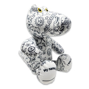 Angled side view of a black-and-white colorable plush frog printed with Florida-themed outlines, showing yellow eyes and a foot panel that reads “My name is.”