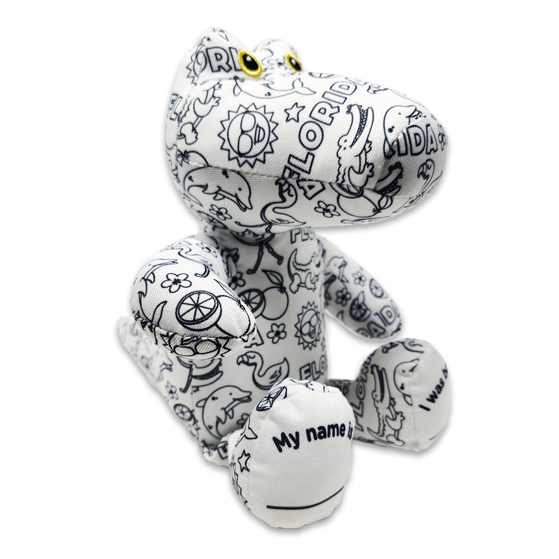Angled side view of a black-and-white colorable plush frog printed with Florida-themed outlines, showing yellow eyes and a foot panel that reads “My name is.”
