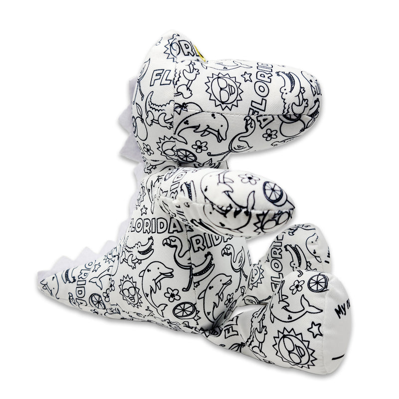 Side view of a black-and-white colorable plush frog printed with Florida-themed outlines, showing yellow eyes and a foot panel that reads “My name is.”