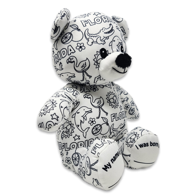 Front angled view of a white teddy bear plush covered in black Florida-themed illustrations, including alligators, flamingos, dolphins, oranges, suns, and the word Florida.
