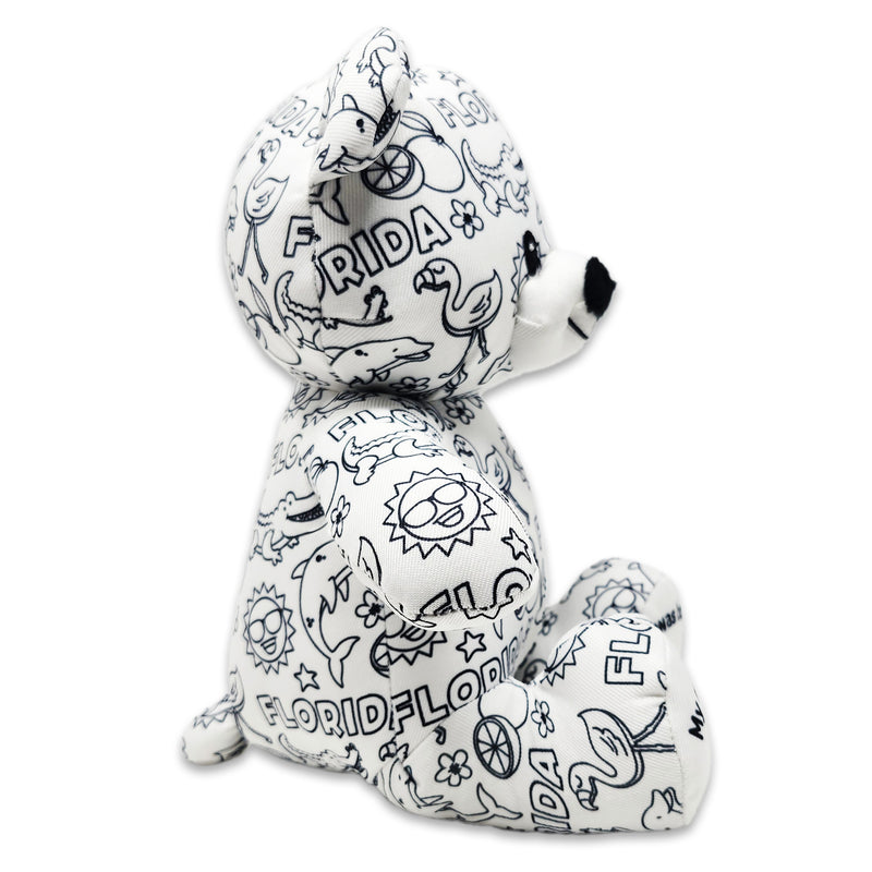 Side view of a white teddy bear plush covered in black Florida-themed illustrations, including alligators, dolphins, flamingos, suns, oranges, and the word Florida.