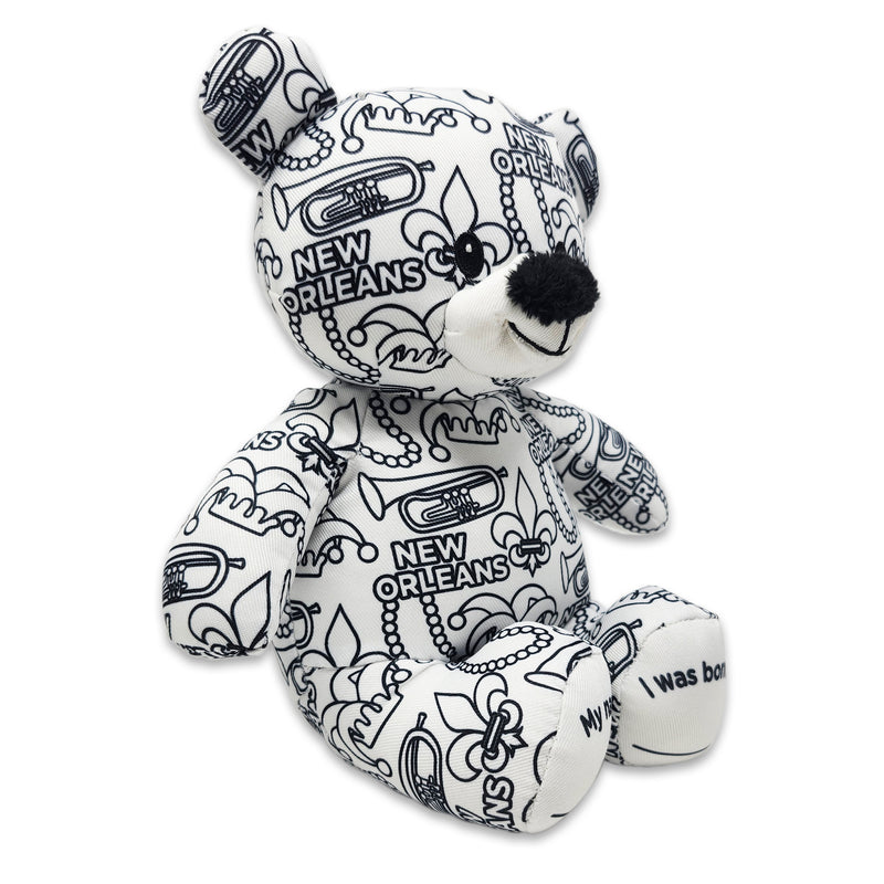 Angle view of a black-and-white colorable plush bear printed with New Orleans text, fleur-de-lis symbols, trumpets, beads, and city-themed designs.