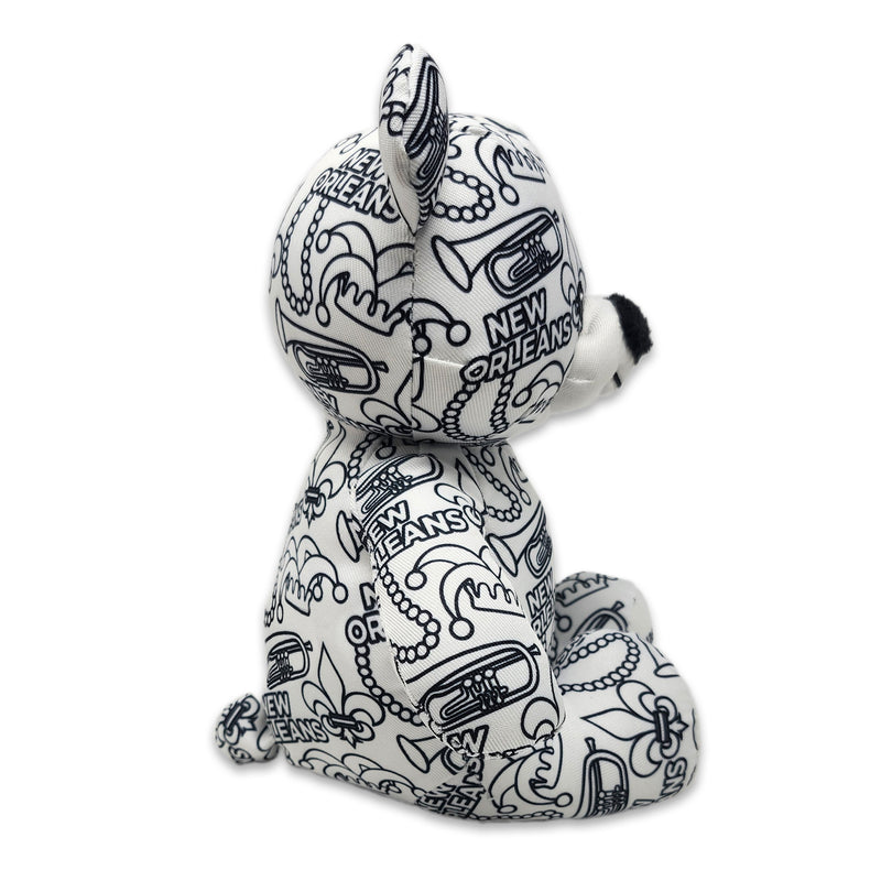 Side view of a black-and-white colorable plush bear printed with New Orleans text, fleur-de-lis symbols, trumpets, beads, and city-themed designs.