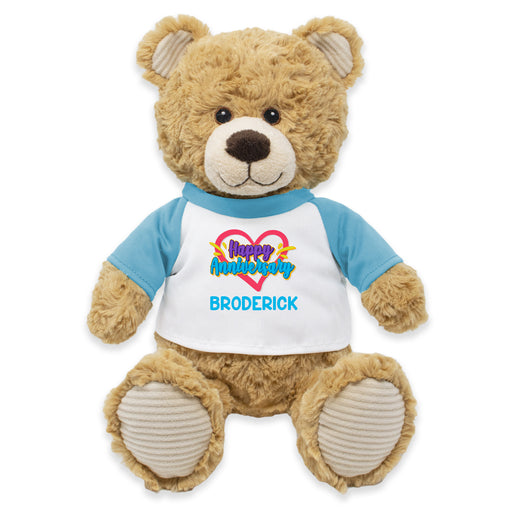A brown plush teddy bear wearing a blue shirt with 'Happy Anniversary Broderick' printed on it.