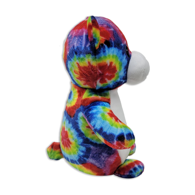 Side view of a tie-dye plush teddy bear with multicolored rainbow fabric, white snout and belly, rounded ears, and seated posture on a transparent background.